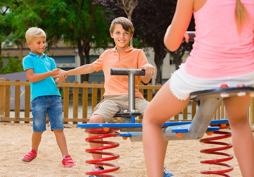 Cheerful american kids are teetering on the swing on the playground.
