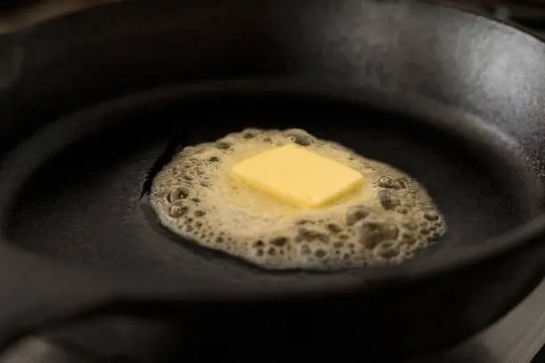 A butter pat melting on a black cast iron frying pan.