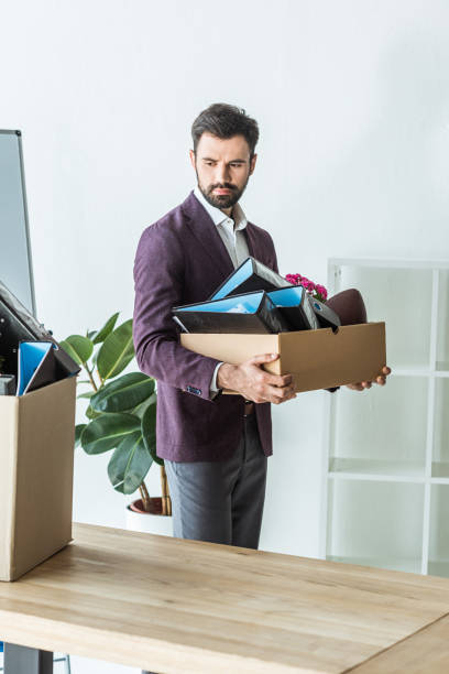 istock fired young businessman carrying box of personal stuff at office 967117230