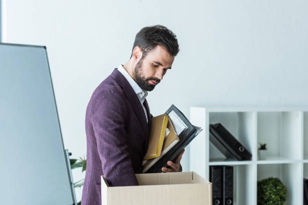 istock fired young businessman putting books and folders into box 967117596