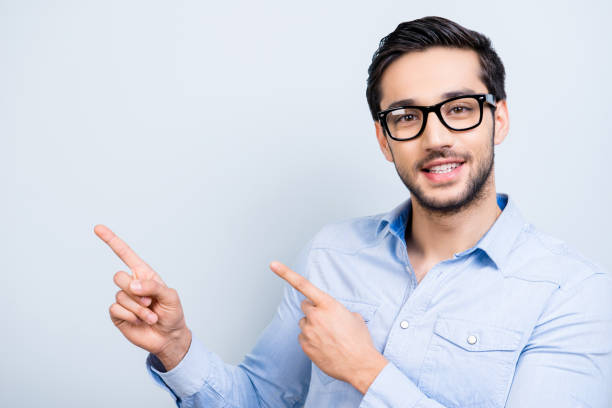istock Portrait with copyspace, cute smiling man with black hair in glasses indicate showing empty place with two forefingers looking at camera isolated on grey background, direction way decision concept 967124418