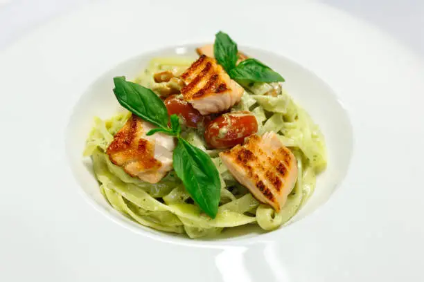Photo of Italian pasta fettuccine with salmon and tomatoes on a white plate