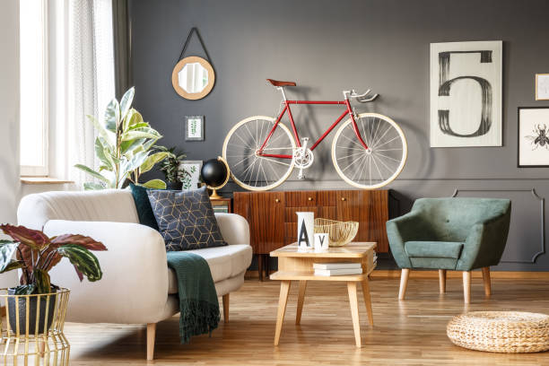 Vintage living room with vibes Vintage unique living room interior with good vibes with white comfortable sofa with cushions and blanket and green armchair, cupboard, small table, red bicycle and lots of details including a poster with number five on gray wall retro bicycle stock pictures, royalty-free photos & images