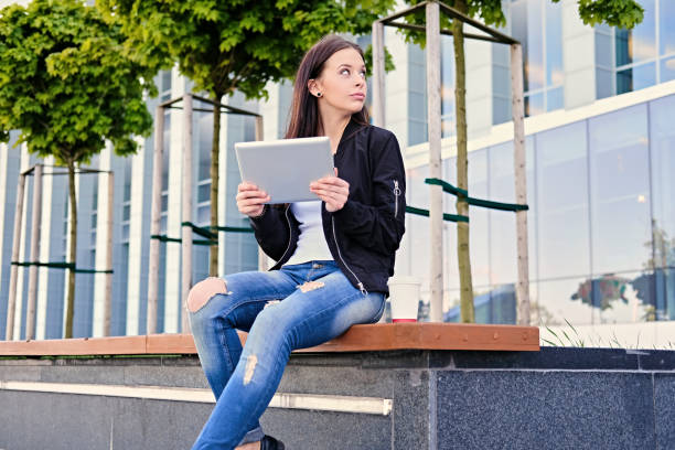 istock Brunette female student using tablet PC on a city street. 967143160