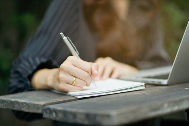 istock close up businesswoman hand writing content or somethings on notebook with using laptop at wooden table outside home , lifestyle concept 967202996