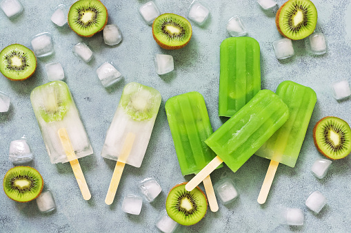 Popsicles kiwi lying on a gray background with ice cubes. The view from above, flat lay. The concept of summer. Summer dessert