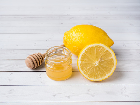 A jar of honey and fresh lemon on white wooden background.
