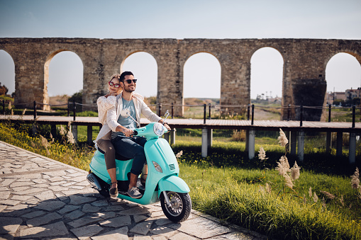 Young loving couple with vintage motorcycle riding next to ancient stone aqueduct monument in Spain