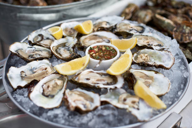 close-up de servidor com bandeja de ostras frescas de concha com fatias de limão, servidas como aperitivo - prepared oysters prepared shellfish shucked seafood - fotografias e filmes do acervo