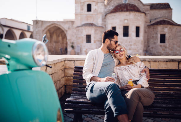Young romantic couple with scooter embracing and relaxing on bench