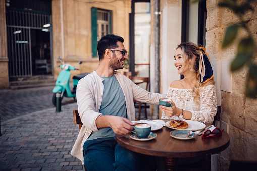 Young happy couple eating breakfast and drinking coffee at stone built coffee shop in Italian streets