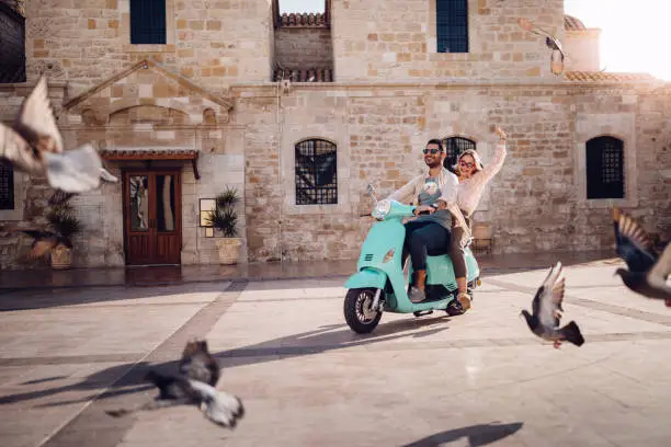 Tourists couple on summer holidays in Italy having fun riding retro scooter in stonebuilt village