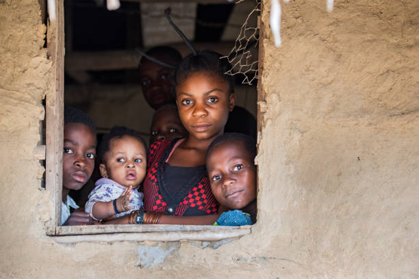 Ndobo, Democratic Republic of Congo - August 27, 2013: : Young Congolese woman with fancy hairstyle togehter with her children, they are looking out of the window of their house at the shores of Congo River.