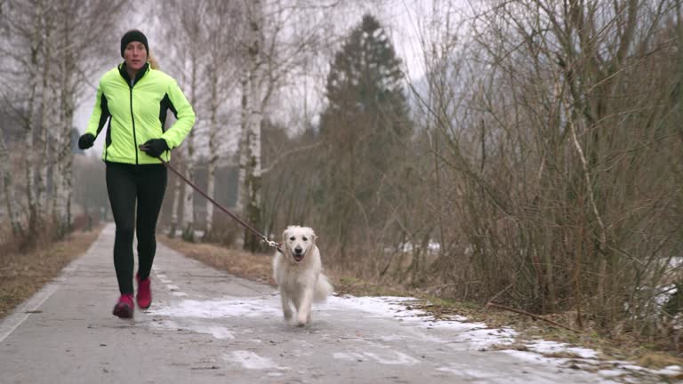 Young Caucasian woman running on a walkway in winter with her dog