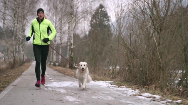 Wide handheld shot of a young Caucasian female running in nature with her dog on a cold winter day. Shot in Slovenia.