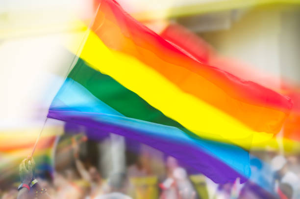 Gay pride rainbow flag flying on a flag pole in double exposure against a street crowded with unrecognizable people