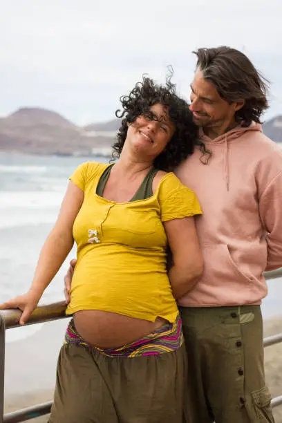 Pregnant woman on yellow shirt and smiling father looking at her on windy day in Las Palmas, Spain