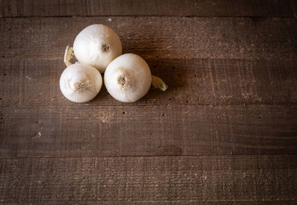 Fresh home grown onions and seasoning herbs on a rustic cooking board with natural morning light in a kitchen.