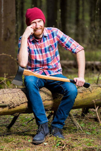 istock happy bearded lumberjack with an ax is sitting on a log in the forest 967374192