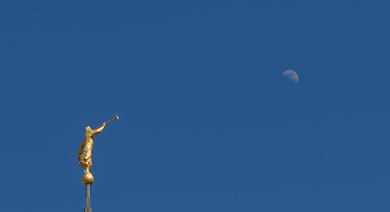 Mormon Angel Moroni Statue against a bright blue sky with the Moon.