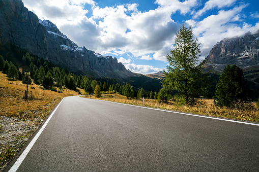 Beautiful mountain road with trees, forest and mountains in the backgrounds. Taken at state highway road in Passo Gardena, Sella mountain group of Dolomites mountain in Italy.