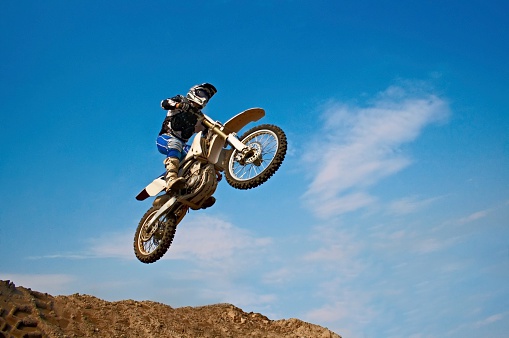 Racer on a cross-country motorcycle in sports equipment in flight after jumping on a springboard, against the blue sky. Kirov, Russia - June 20, 2021