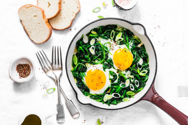 istock Green shakshuka. Fried eggs with fresh spinach, ramson, leek in a cast iron skillet on a white background, top view 967510252