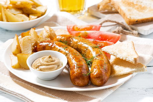 fried sausages with potatoes and mustard on plate, closeup