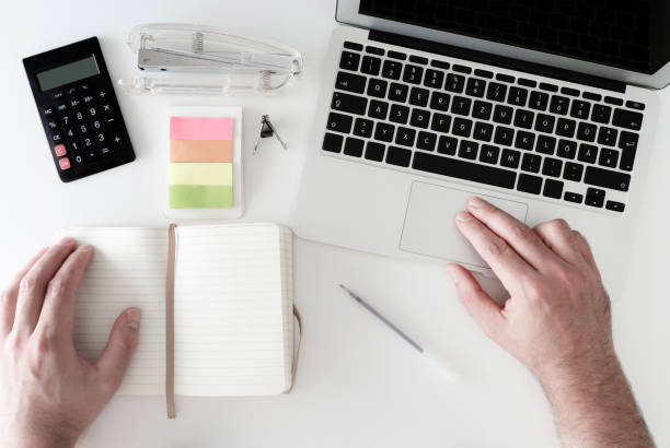 istock overhead shot of man working on notebook computer on white desk cluttered with office supplies 967646818