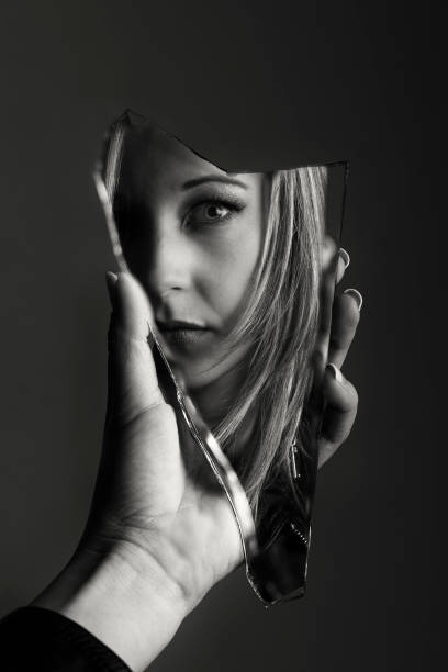 Woman looking at her face in a shard of an broken mirror artistic conversion - fotografia de stock