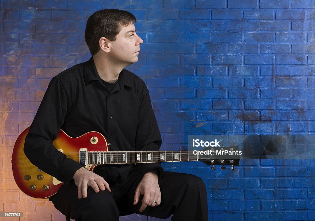 Man with Guitar on Lap Man sitting with guitar on his lap in front of blue brick wall 30-39 Years Stock Photo