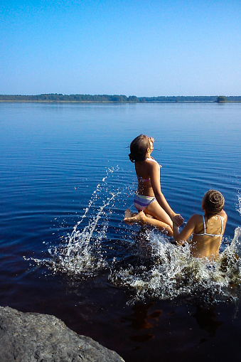 Children jumping from stone beach to beautiful blue lake. Having fun with your friends on summer vacation.