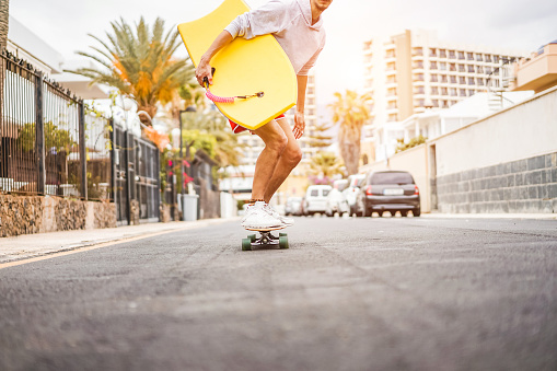Young man riding longboard around city streets - Skater having fun going with skateboard - Youth lifestyle and millennial trend concept - Focus on body
