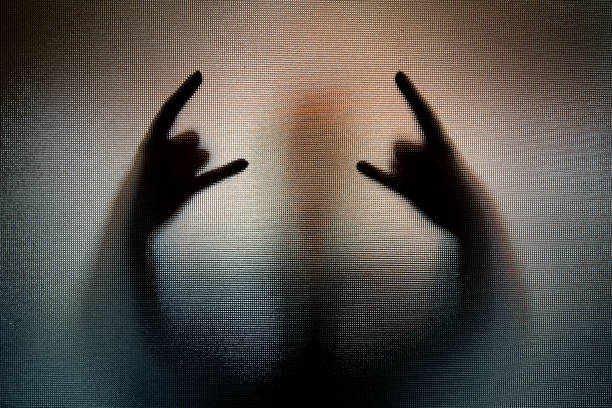 Silhouette of heavy metal horn sign hand gesture Color image depicting the shadow silhouette of a person performing the heavy metal sign of the horns hand gesture, behind frosted glass. The person's body is distorted and spooky, giving an atmospheric, mood to the image. Lots of room for copy space. heavy metal stock pictures, royalty-free photos & images