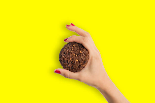 istock Brown cookie on bright yellow background holding by woman hand 967766370