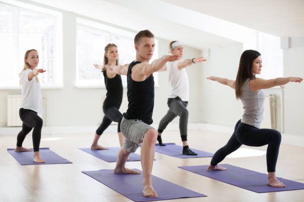 istock Group of young sporty people in Warrior Two exercise 967775136