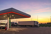 Side view of gas station fueling with cars standing on it and white truck at sunset or early morning time.