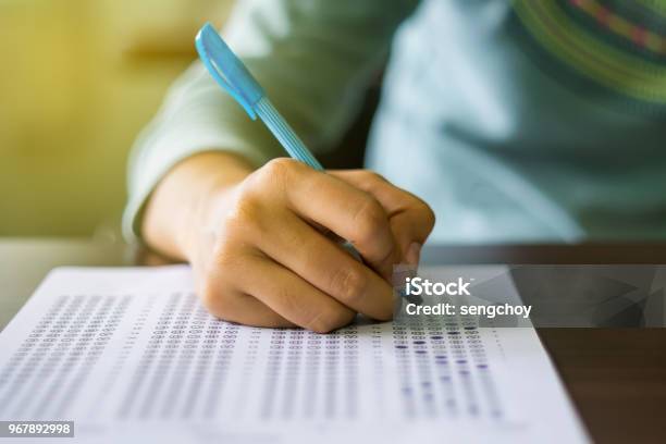 Close Up Of High School Or University Student Holding A Pen Writing On Answer Sheet Paper In Examination Room College Students Answering Multiple Choice Questions Test In Testing Room In University Stock Photo - Download Image Now