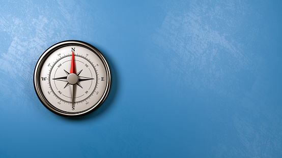 Metallic Compass with Red Magnetic Needle Pointing Toward the North Against a Plastered Blue Wall with Copyspace, 3D Illustration