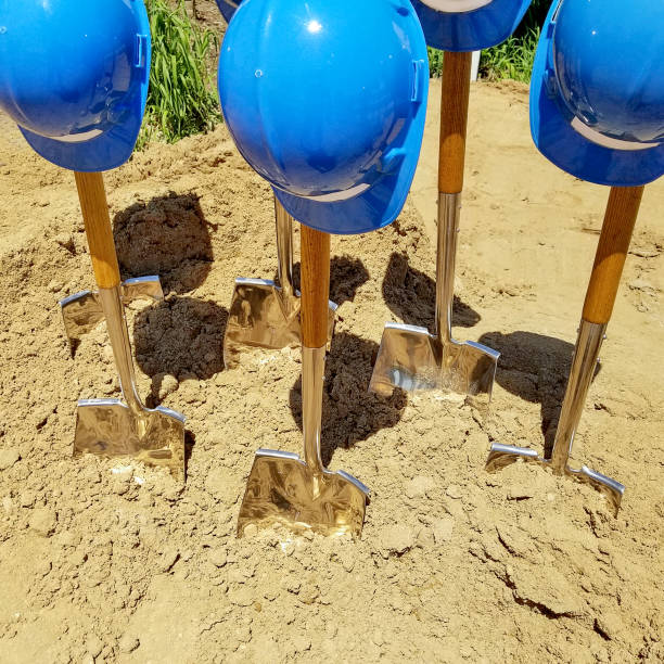 blue hard hats on shiny shovel stuck in dirt for ground breaking ceremony