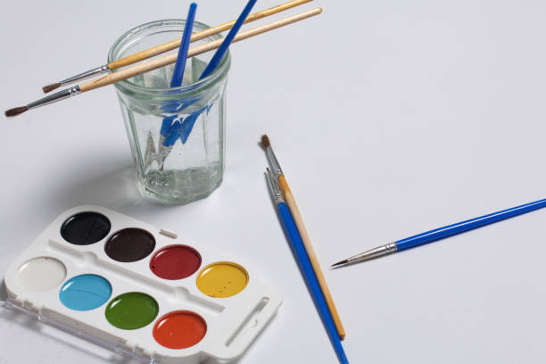 istock Watercolors and brushes on a white surface. Next glass for water. Subjects for creativity. 967929274