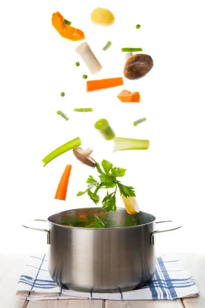 Fresh vegetables to cook a soup falling into a pot isolated on a white background