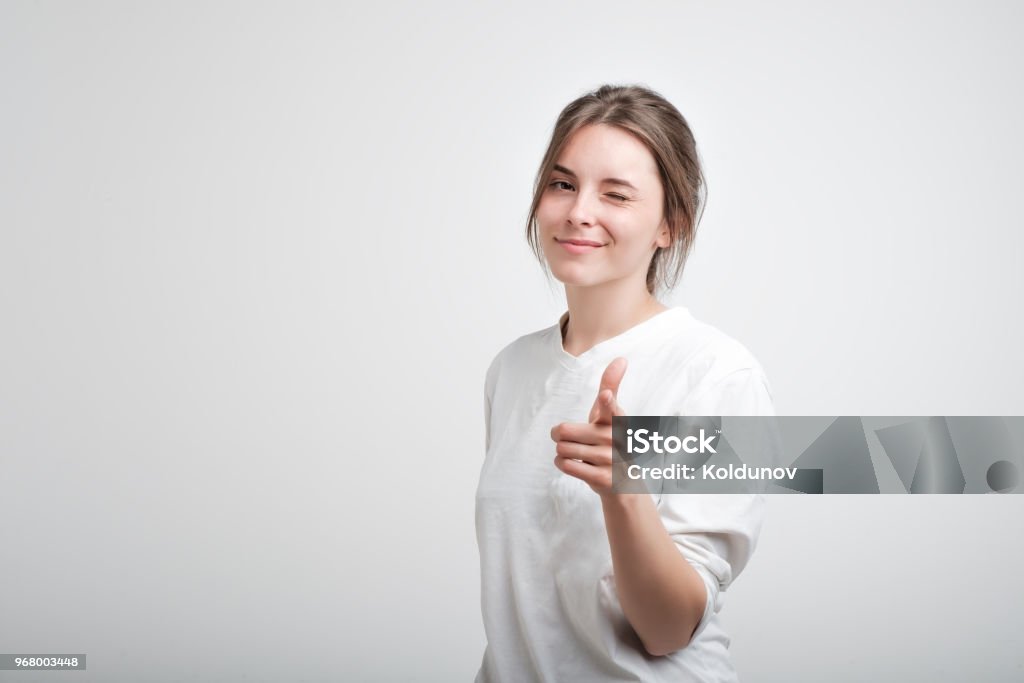 Positive fröhliche Junge kaukasischen Frau tragen weiße lässigen T-Shirts, blinzelte und lächelt in die Kamera zeigen - Lizenzfrei Frauen Stock-Foto