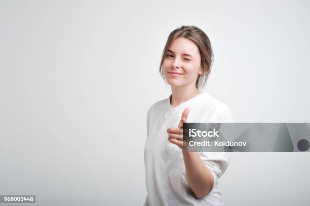 Positive Cheerful Young Caucasian Woman Wearing White Casual Tshirt Blinking Her Eyes And Smiling Pointing At Camera Stock Photo - Download Image Now