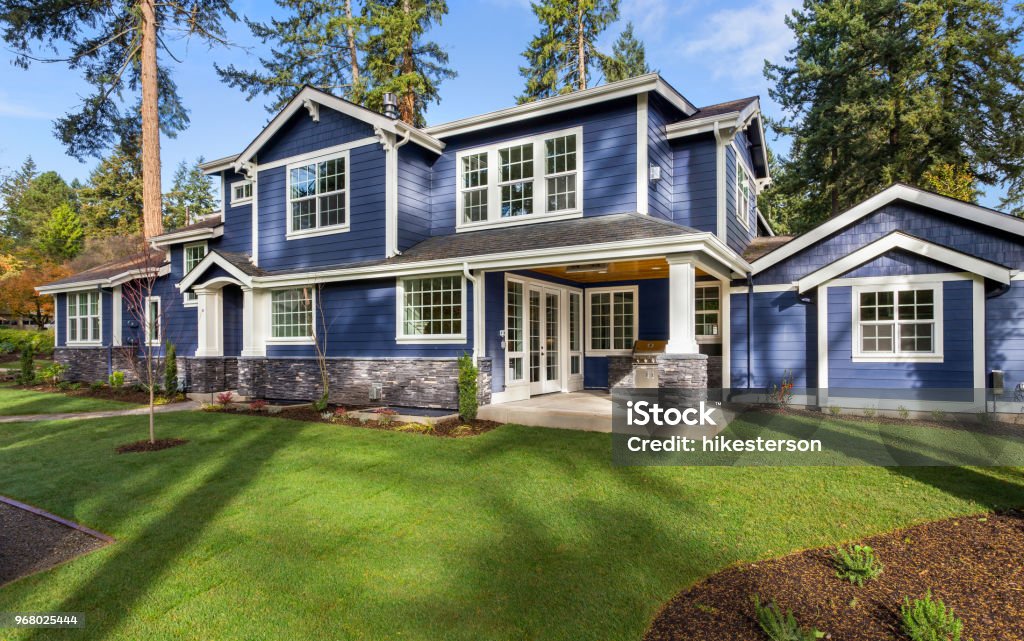 Beautiful luxury home exterior on bright sunny day with green grass and blue sky facade of home with manicured lawn, and backdrop of trees and blue sky House Stock Photo