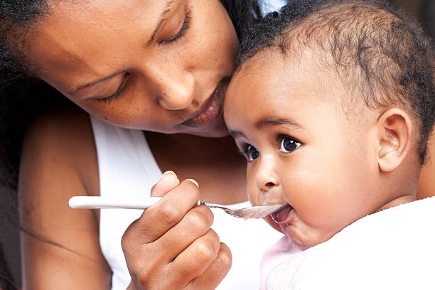 Mother feeding her baby Mother feeding her 5 month old baby with a spoon. ethiopian ethnicity photos stock pictures, royalty-free photos & images