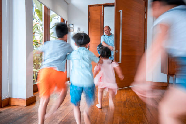 Father is hugging his children at the front door after coming home. They are happy.
