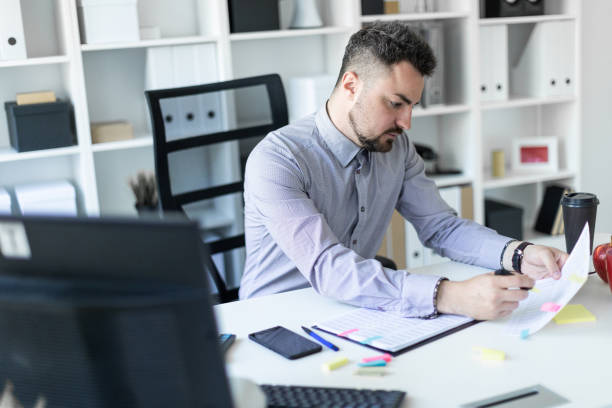 istock A young man in the office sits at a table, holds a marker in his hand and works with documents. 968086360