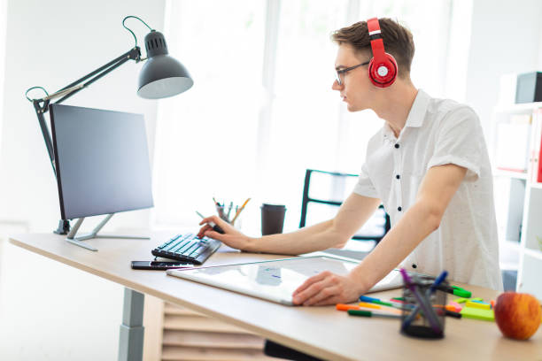 istock A young man with glasses and headphones is working at the computer. Before the guy is a magnetic board and markers. 968086378