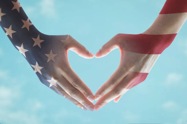 istock America flag pattern on people's hands in heart shape on blue sky background 968086436